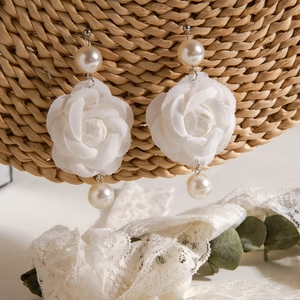 Détails de boucles d'oreilles fleurs en tissu blanc avec perles sur panier en paille