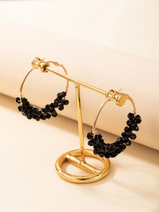 Détail de créoles dorées avec perles noires facettées sur un présentoir à bijoux