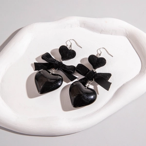 Détail de boucles d'oreilles cœur en velours noir avec nœud et pendentifs en résine