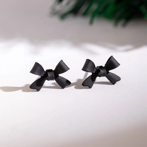 Détail de boucles d'oreilles nœuds noir mat sur une surface gris clair texturée