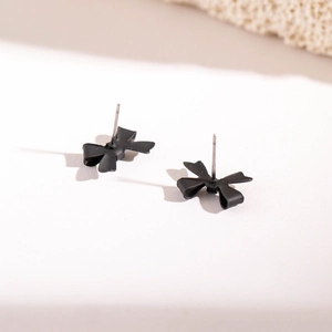 Détail des boucles d'oreilles nœud papillon noir mat sur fond blanc minimaliste