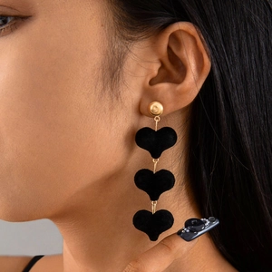 Détail de boucles d'oreilles pendantes avec trois cœurs en velours noir sur chaîne dorée