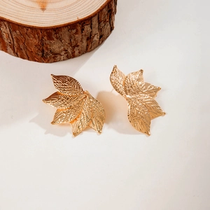 Gros plan détaillé de boucles d'oreilles feuille dorée avec textures de veines sur bois