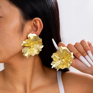 Gros plan de grandes boucles d'oreilles dorées en forme de fleur avec texture miroir