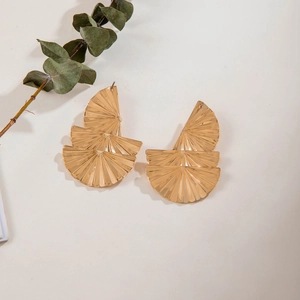 Détail de boucles d'oreilles dorées en éventail avec texture radiale et design floral