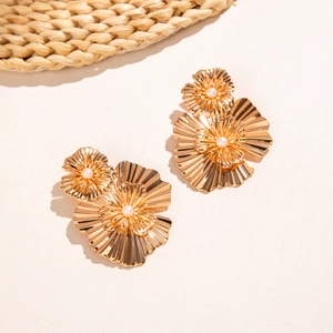 Détail de boucles d'oreilles fleur dorées texturées avec des accents de perles