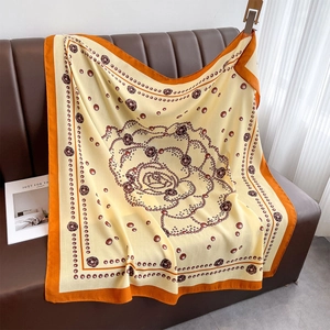 Detail view of large square silk scarf with rose floral print on a leather sofa