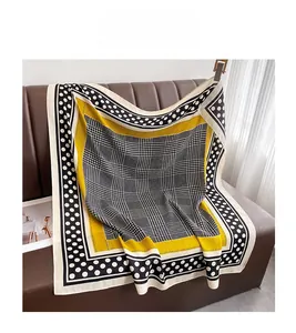 Détail d'un foulard en soie à motif pied-de-poule et bordure jaune sur un canapé en cuir