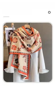 Détail d'une écharpe en imitation cachemire avec motifs floraux et pompons orange vif