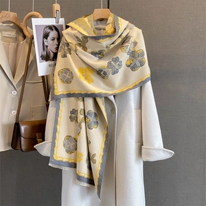 Écharpe beige avec imprimé floral jaune et franges sur un cintre en bois