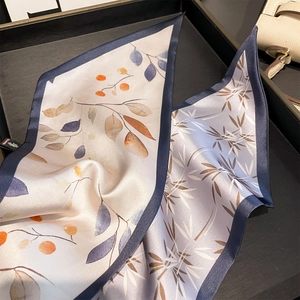 Élégant foulard en soie à imprimé floral et baies présenté sur un sac à main chic