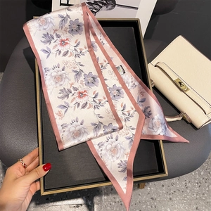 Elegant floral print skinny silk scarf draped in a display tray with a beige handbag