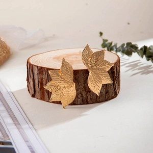 Boucles d'oreilles dorées en forme de feuille avec texture vintage sur bois naturel