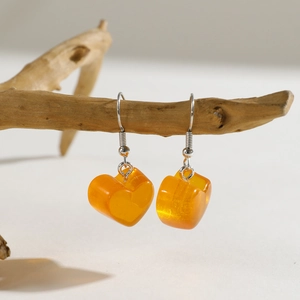 Detailed view of amber heart resin earrings hanging on a natural wooden branch