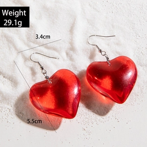 Translucent red heart pendant earrings with silver hooks on a textured white background