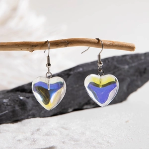Detail of heart earrings with blue and yellow resin texture on a wooden branch stand