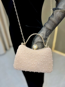 Detail of elegant pearl evening clutch with gold handle and chain on velvet background
