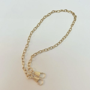 Detail of light gold oval metal chain with spring hooks for bags and masks