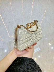 Elegant pearl evening handbag with diamond bow design and golden handle held by model