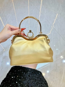 Detail of golden pleated evening clutch bag with round metal handle on marble surface