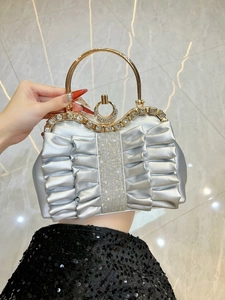 Macro detail of silver pleated evening bag featuring shimmering rhinestones and gold ring handle