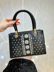 Close-up of black snakeskin texture handbag with floral rhinestones and braided handle