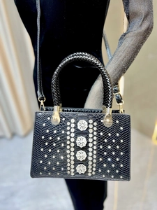Detail view of a black crocodile-embossed handbag featuring luxury rhinestone flower accents