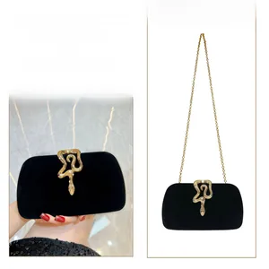 Detail of black velvet evening clutch featuring gold snake buckle and chain strap