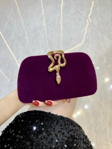 Detailed view of dark purple velvet evening clutch with a golden snake-shaped rhinestone buckle