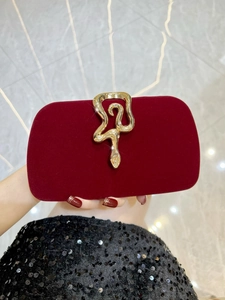 Detail of red velvet clutch bag featuring luxury golden snake shaped metal buckle closure