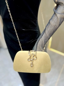 Detail of velvet evening clutch with gold snake clasp and chain strap against black dress