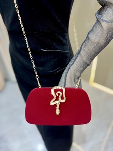 Detail of red velvet clutch with golden snake-shaped clasp and delicate chain strap