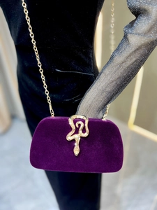 Macro detail of golden snake-shaped buckle on luxury purple velvet evening clutch bag