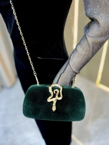 Detail of green velvet evening clutch featuring a gold snake-shaped clasp and chain strap