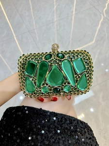 Close-up of luxury evening clutch with green emerald-cut gems and gold filigree metalwork