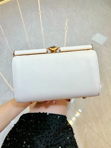 Close-up of a white leather evening clutch bag with gold hardware and jewel clasp