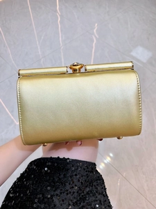 Detailed view of golden evening clutch with large gemstone clasp and protective metal feet