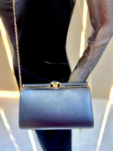 Detailed view of black leather clutch with jewel clasp and gold chain strap