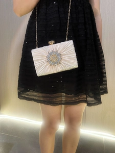 Detail of pleated evening clutch with sparkling sunflower rhinestone and gold chain strap