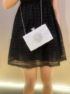 Close-up of pleated satin evening clutch with sparkling rhinestone flower and gold chain