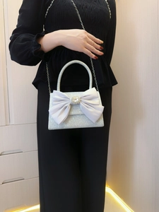 Detail of silver sequin evening bag featuring a white satin bow and rhinestone buckle