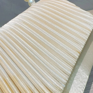 Close-up of champagne pleated satin evening clutch with elegant pearl clasp detail