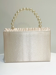 Detail of champagne gold evening bag with satin pleats and large pearl handle