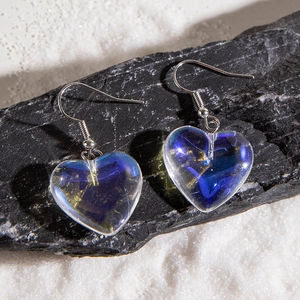 Macro detail of transparent heart pendant earrings with iridescent purple core on black rock