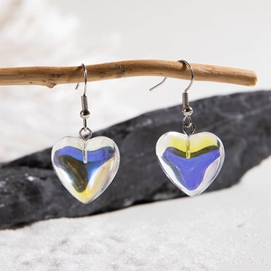 Detail of heart-shaped gradient glass earrings hanging on a natural wooden branch