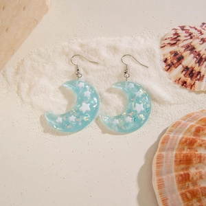 Resin crescent moon earrings with stars and glitter on a beach sand background