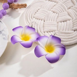 Détail de boucles d'oreilles fleur de frangipanier violettes sur texture tressée