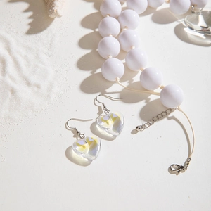 Détail de boucles d'oreilles cœur et collier de perles blanches sur fond de plage de sable blanc