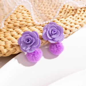Detail of purple rose earrings with soft pom-pom drops on textured rustic surface