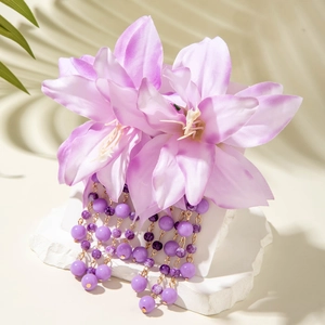 Detail of purple floral tassel earrings with beaded chains on a white stone pedestal